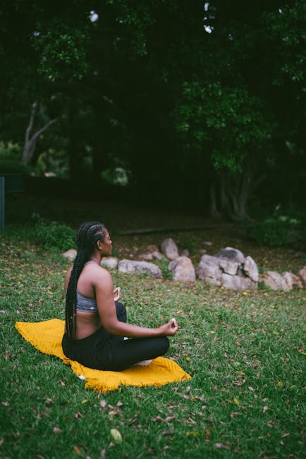 A woman meditating on a yellow mat in a serene outdoor setting.