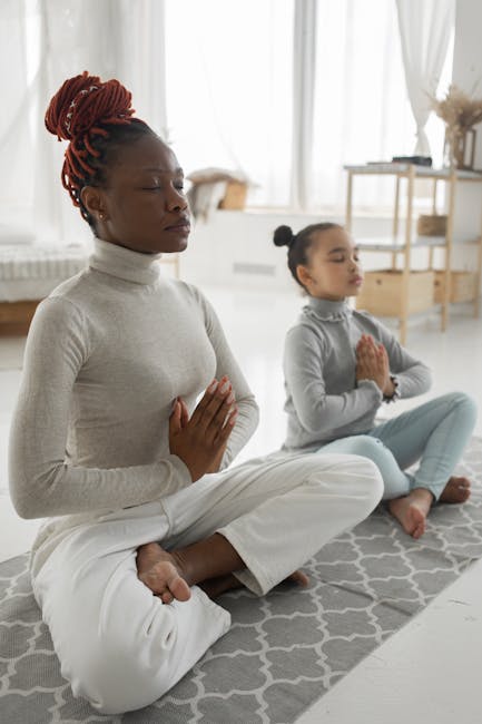 Full body of tranquil young barefooted African American woman in casual clothes sitting on carpet in Padmasana pose with closed eyes while meditating with adorable little daughter at home